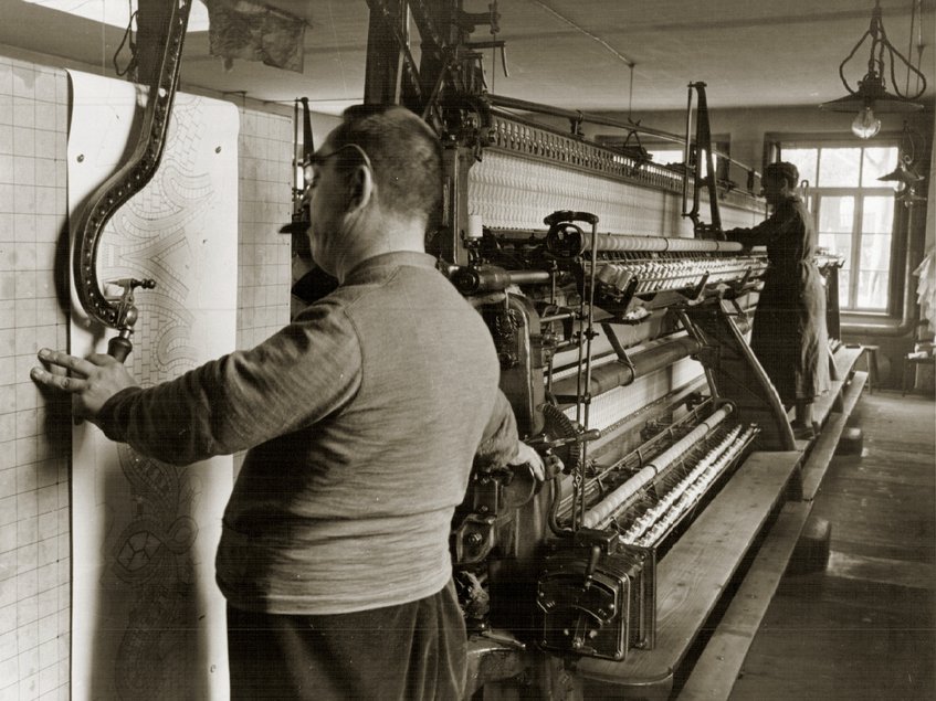 Schwarzweisfoto eines Stickers an einer historischen Stickmaschine