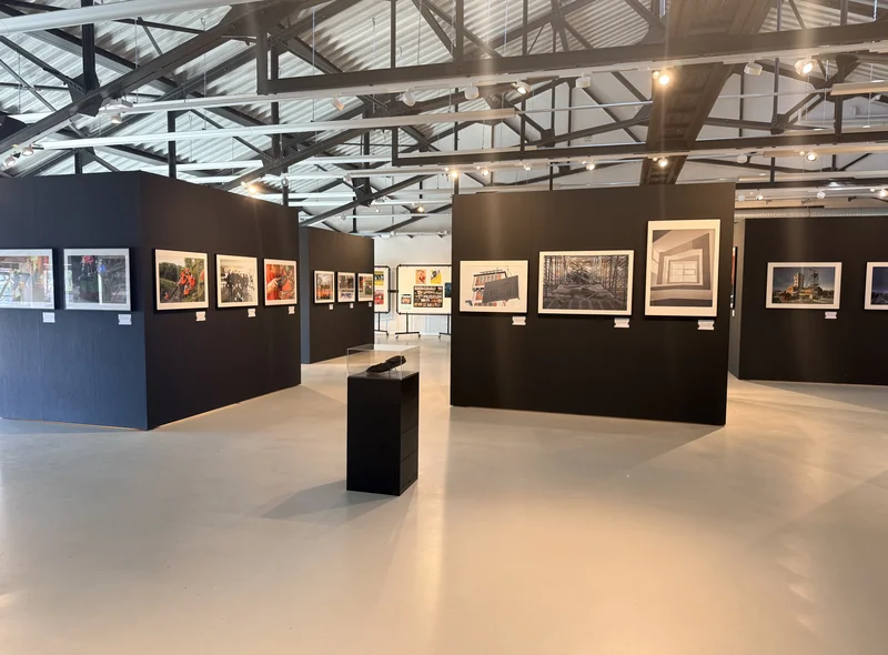 Großer Raum mit schwarzen Ausstellungswänden, an denen großformatige Fotografien präsentiert werden