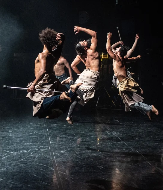 Momentaufnahme von vier sich auf einer Bühne bewegenden Tänzern in modern wirkenden Kostümen