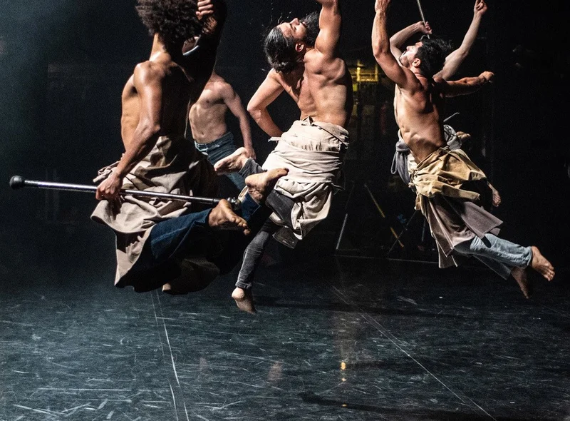 Momentaufnahme von vier sich auf einer Bühne bewegenden Tänzern in modern wirkenden Kostümen