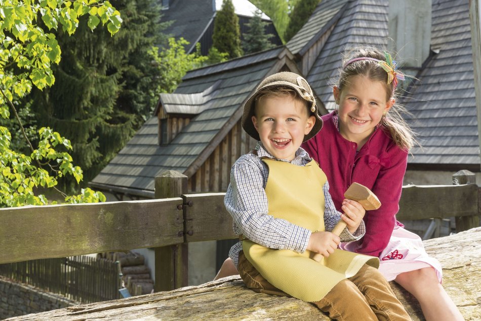 Das Foto zeigt einen Jungen und ein Mädchen fröhlich auf einer Bank vor dem Frohnauer Hammer sitzend.