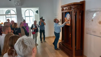 Museumsbesucher beobachten den Uhrmachermeister an der Astronomischen Kunstuhr in ihrem historischen Korpus in Schrankgröße