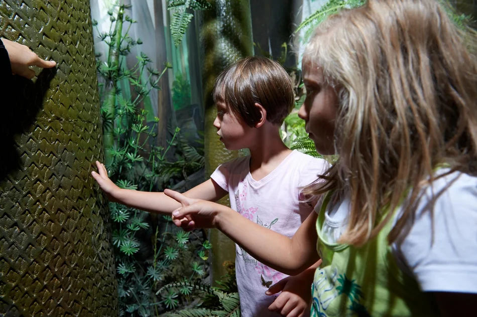 Steinkohlenwald Zwei Kinder stehen in der Inszenierung eines Urwaldes und betrachten aufmerksam einen nachgebildeten Baumstamm.
