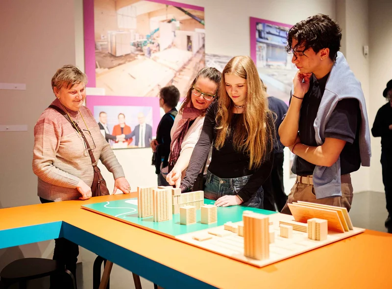 Besucherinnen und Besucher betrachten ein Tastmodell von Plattenbauten in der Ausstellung.