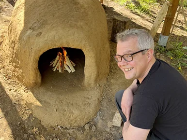 Lehmofen Das Bild zeigt einen Mann vor einem Lehmofen. Im Ofen brennt Feuer.