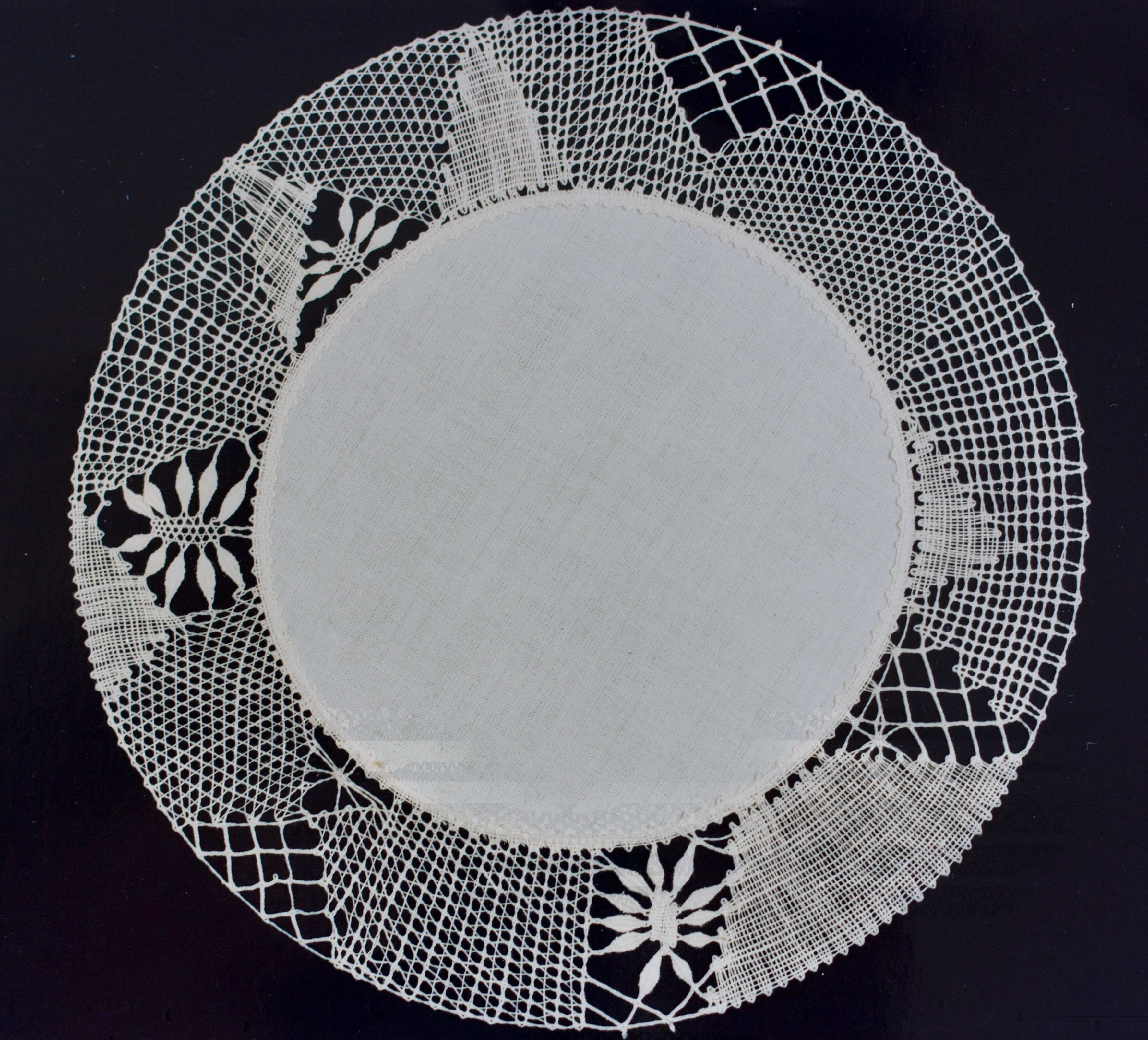Weißes rundes Deckchen mit einer kunstvoll gestalteten Klöppelspitzen-Umrandung