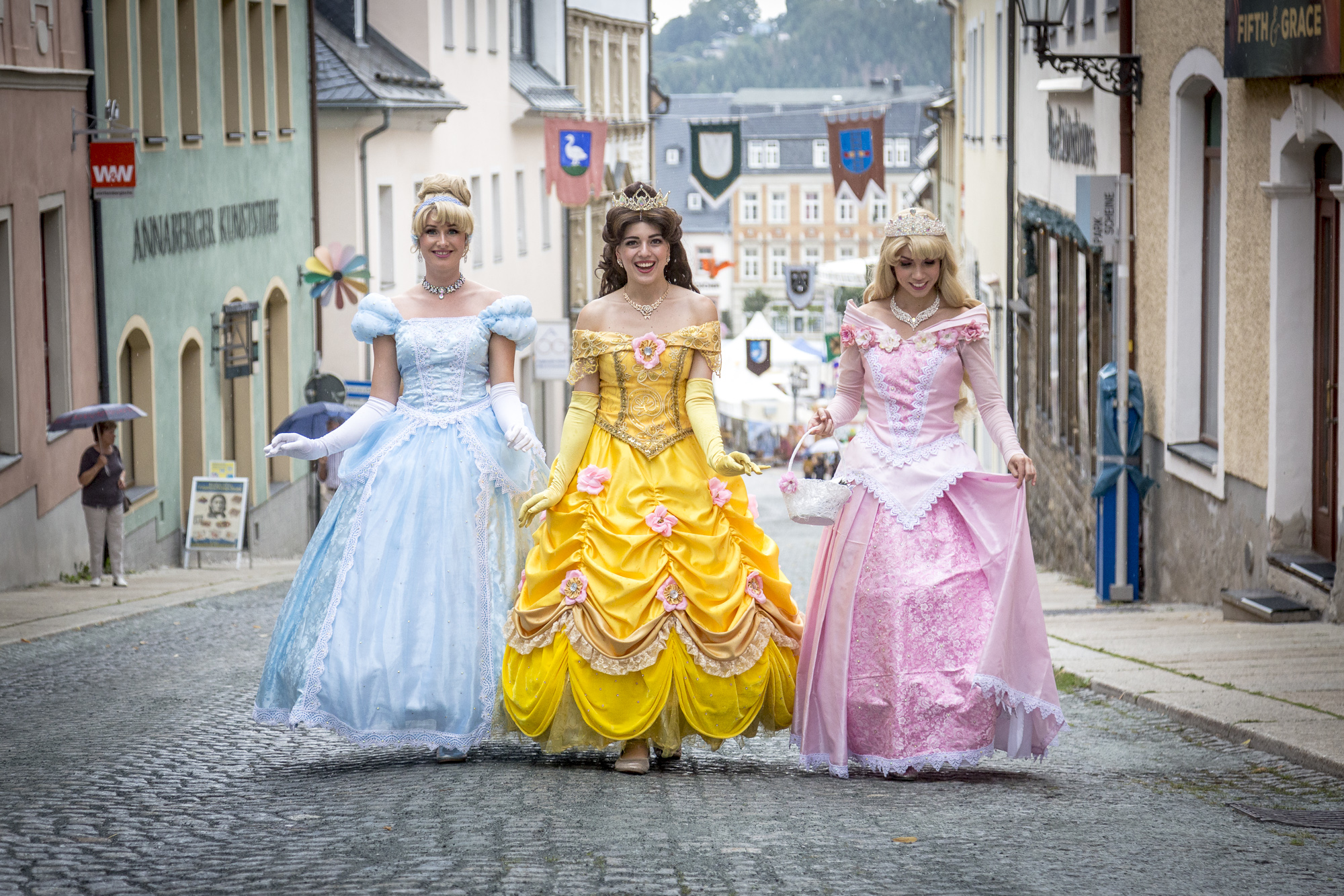 Foto dreier als Prinzessinnen verkleideter junger Frauen in historischer Kopfsteinpflaster-Gasse