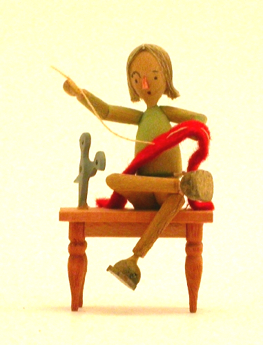 Holzfigur eines Schneiders, der auf einem Holzstühlchen sitzt und mit gelbem Faden einen roten Stoff näht