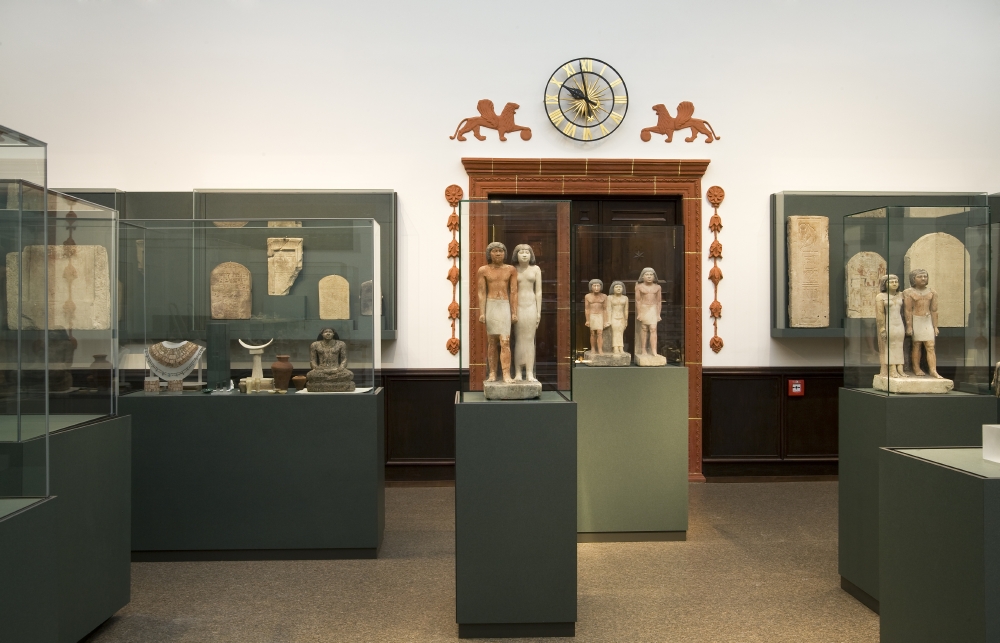 Das Foto zeigt eine mehrere Vitrinen, zentral eine Statue eines Ehepaares, in der Eingangshalle des Ägyptischen Museums Georg Steindorff.