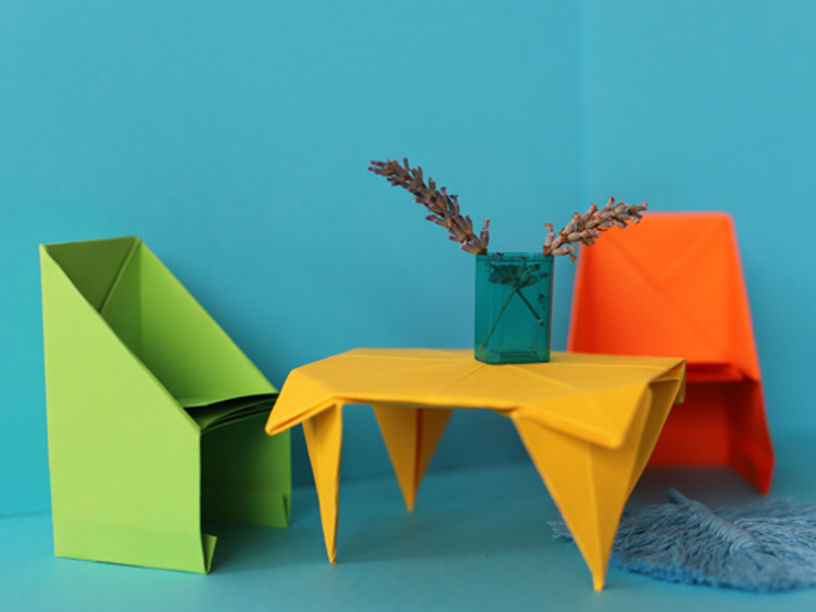 Das Bild zeigt bunte Origami-Möbel vor einem blauen Hintergrund.