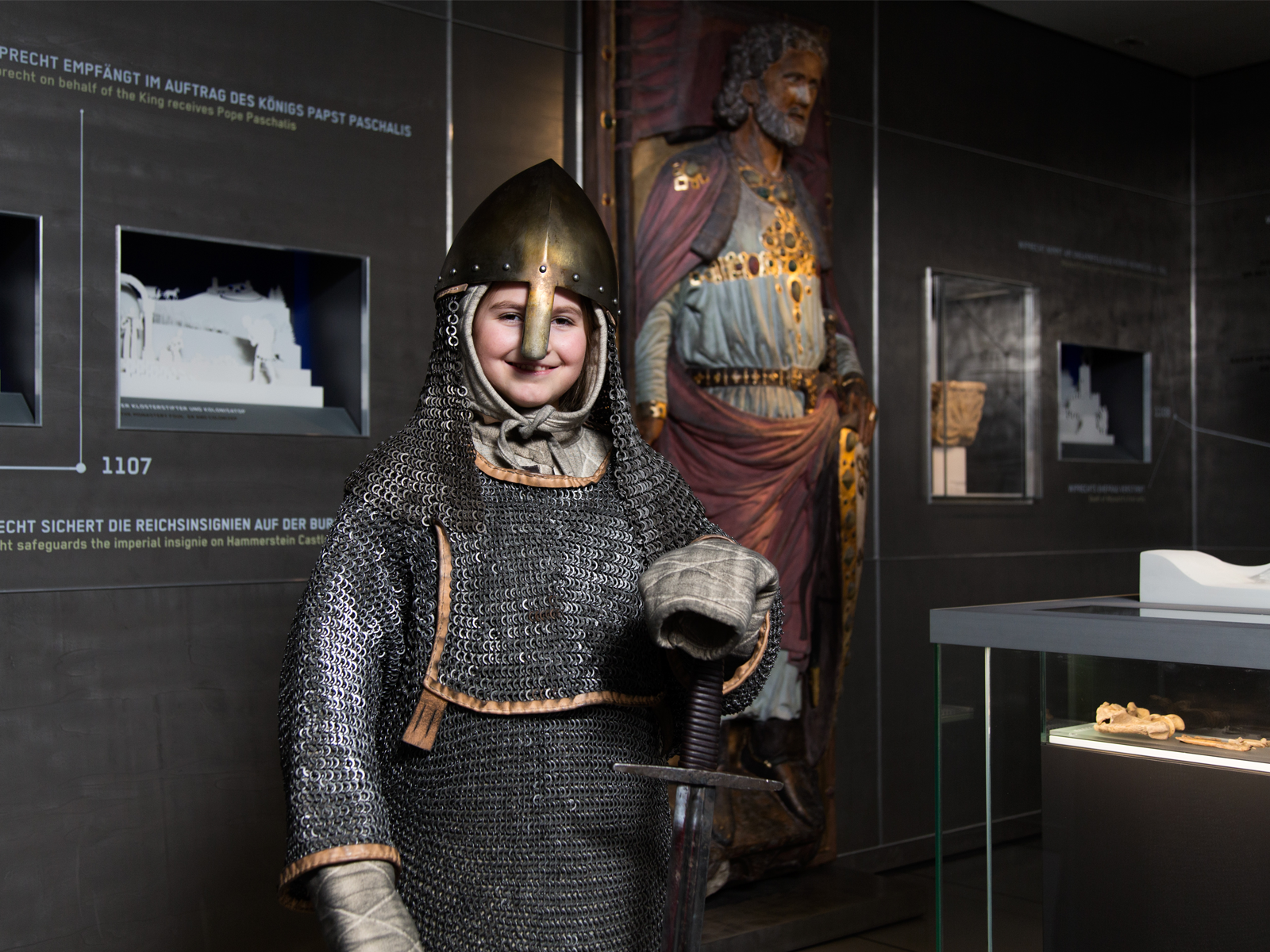 Auf dem Bild ist ein Kind in einer Ritterrüstung zu sehen. Im Huntergrund sind Exponate des Museums zu sehen.