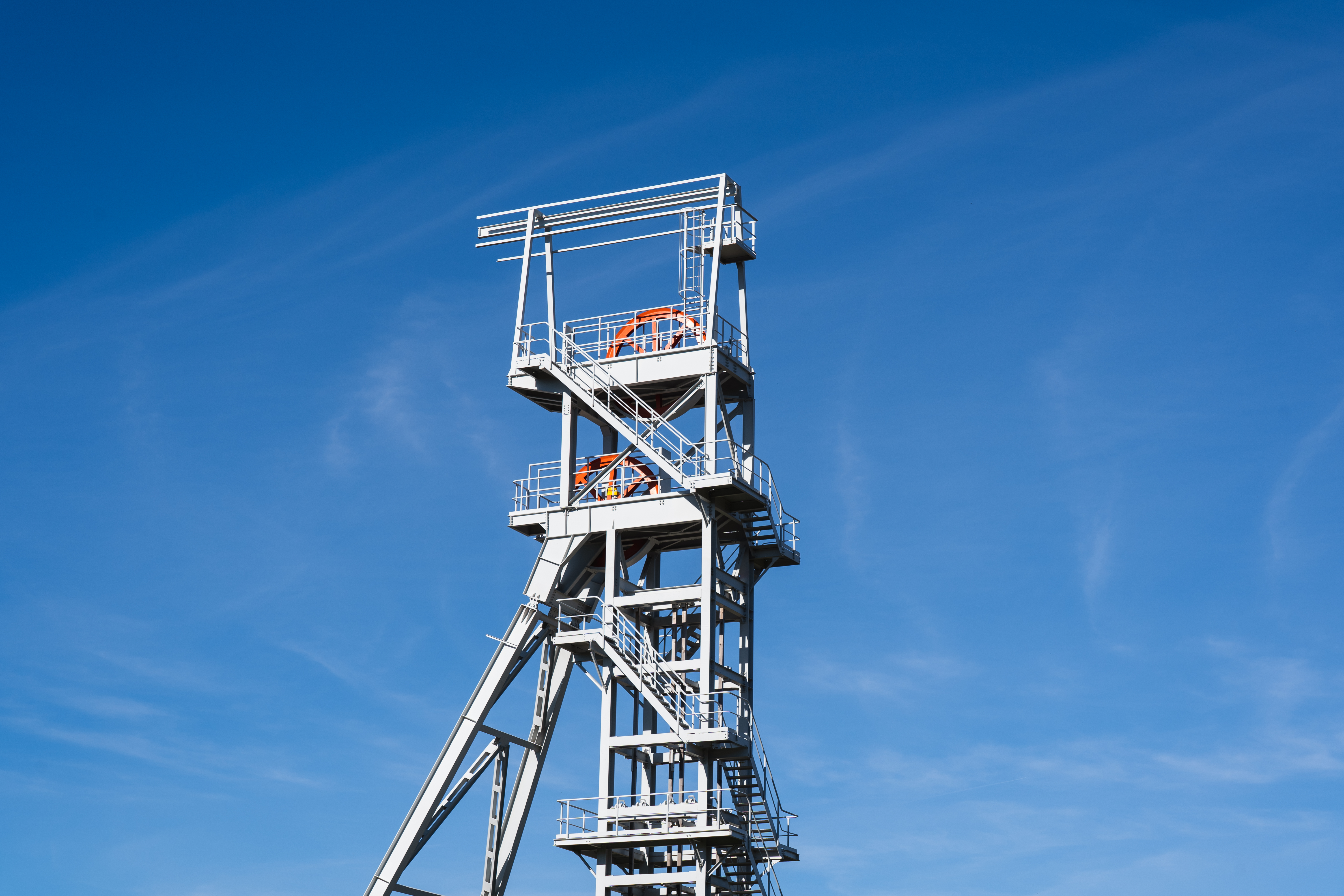 Stahlgerüst eines Förderturms mit roten Rädern vor strahlend blauem Himmel