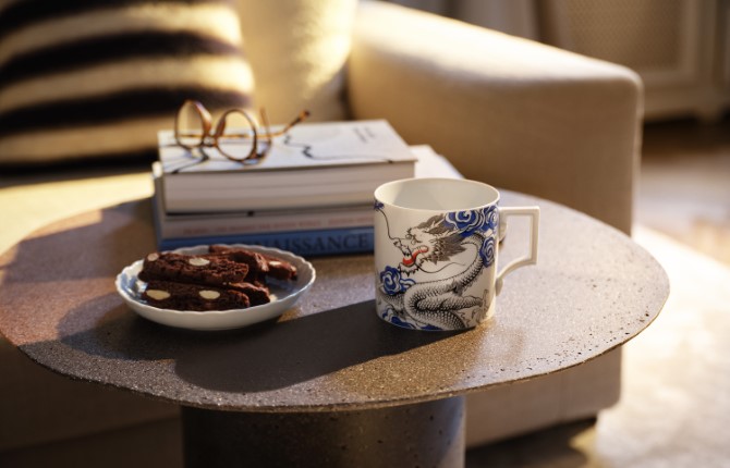Auf einem kleinen, runden Couchtisch liegt ein kleiner Bücherstapel mit einer Brille obendrauf, daneben ein Schälchen mit Gebäck und eine fein bemalte Tasse aus Meissener Porzellan.