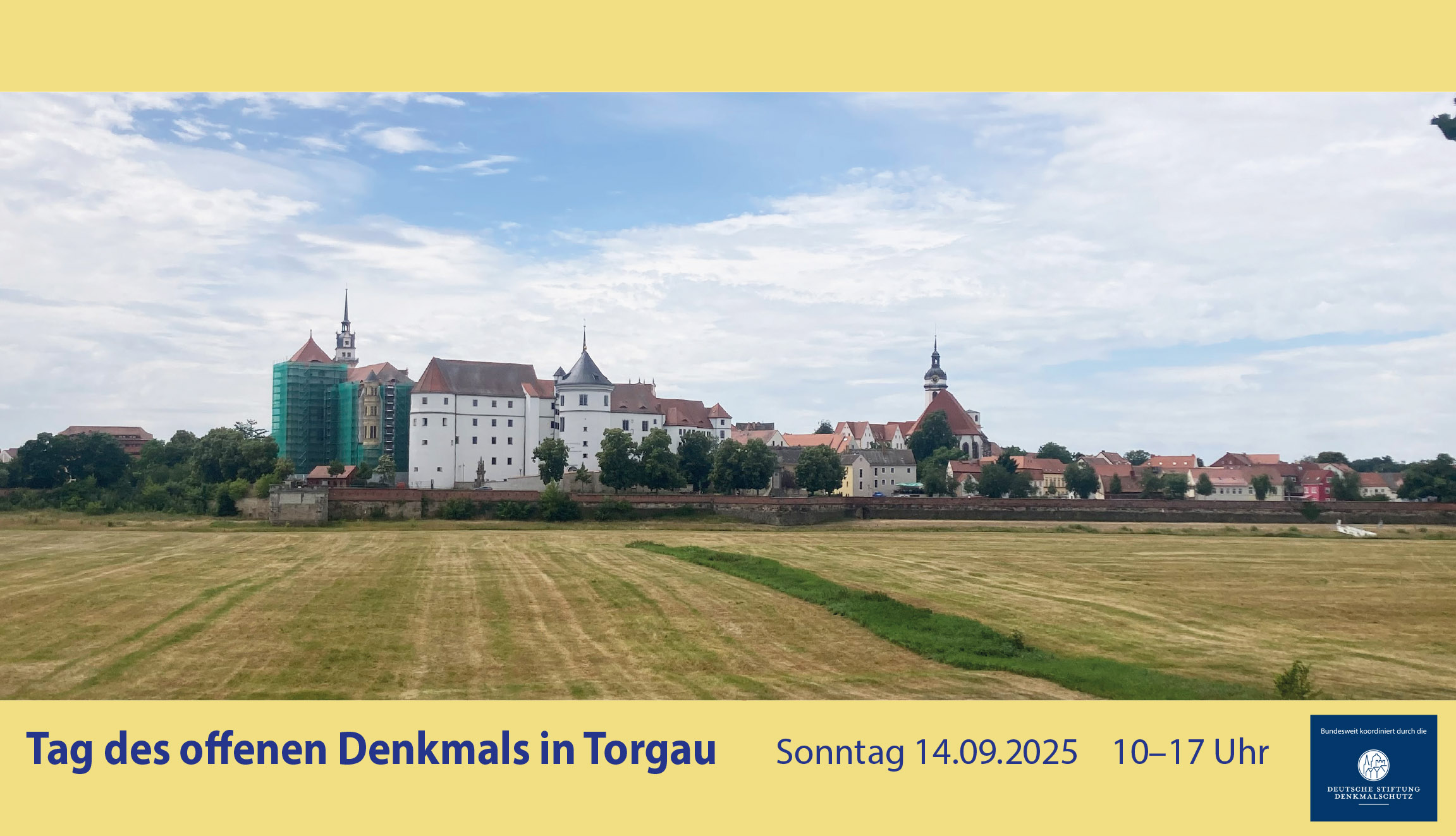 Panorama-Foto über abgemähte Wiesen hin zu einem großen Schloss mit weißer Fassade und mehreren Türmen