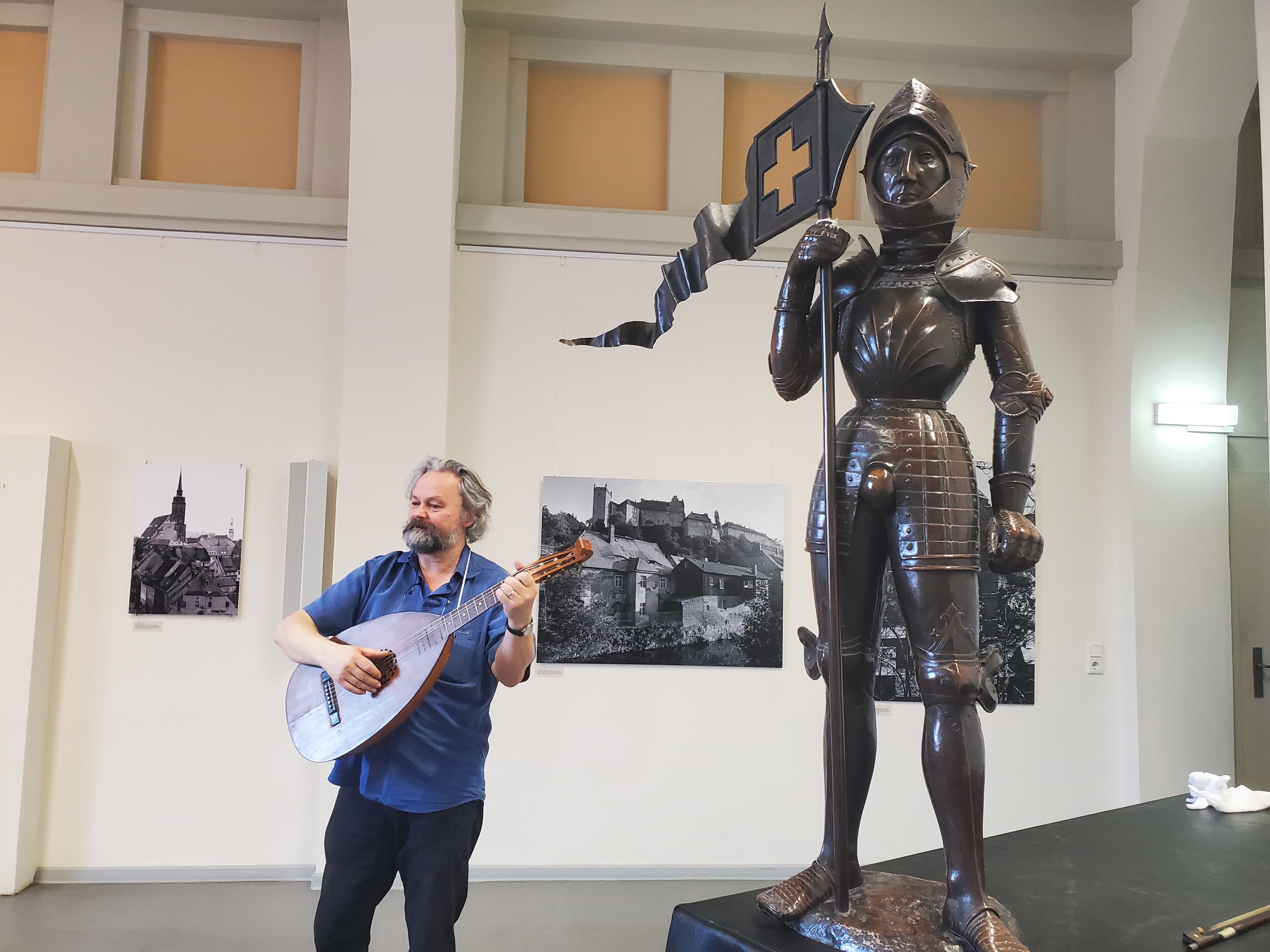 In einen Museumsraum steht auf er linken Seite das Modell eines Ritters, während auf der rechten Seite ein Mann eine Laute spielt.