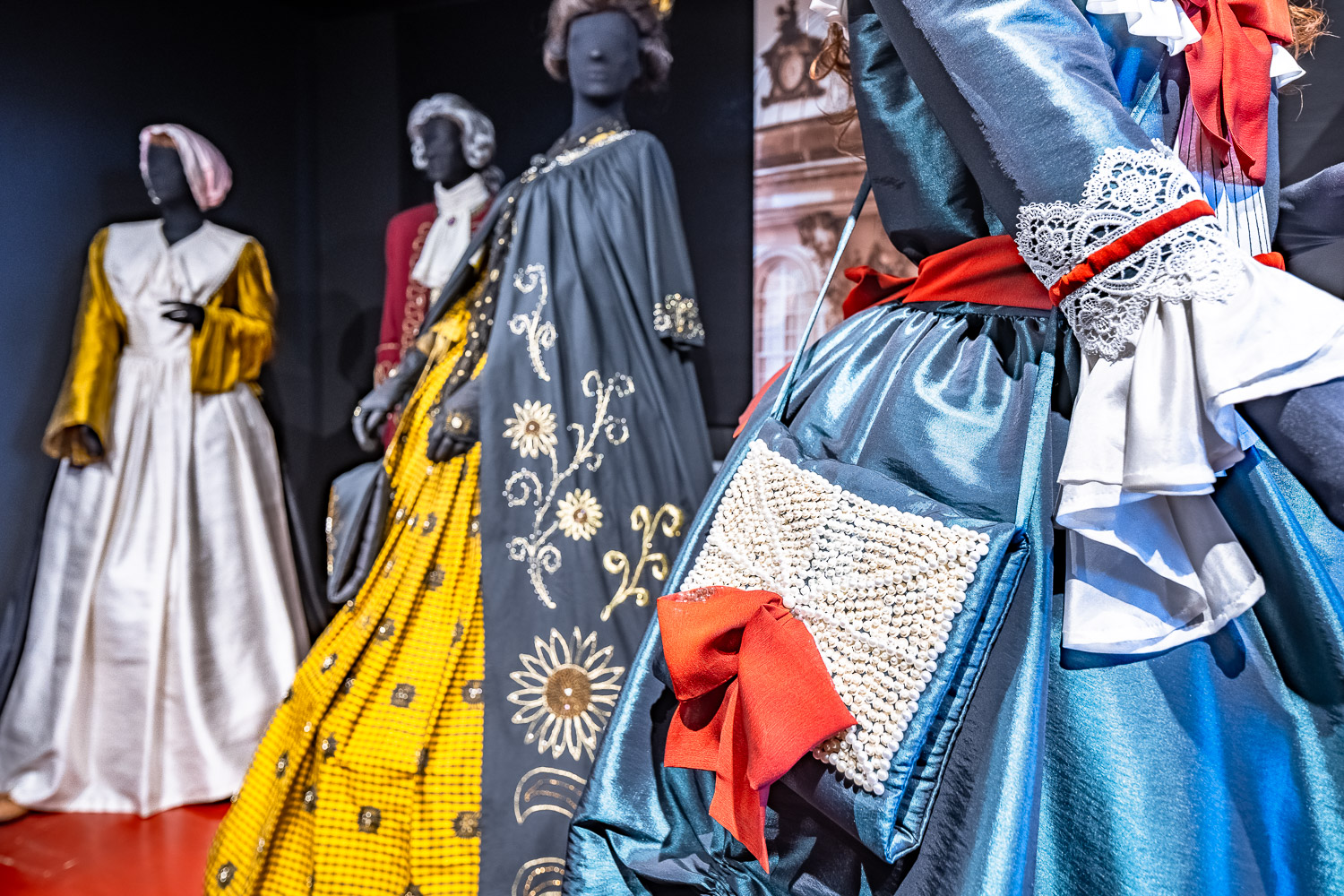 Das Foto zeigt vier in der Dauerausstellung zu 1000 Jahren Modegeschichte gezeigte reich verzierte, farbenfrohe Kleider beziehungsweise Roben aus vergangenen Jahrhunderten.