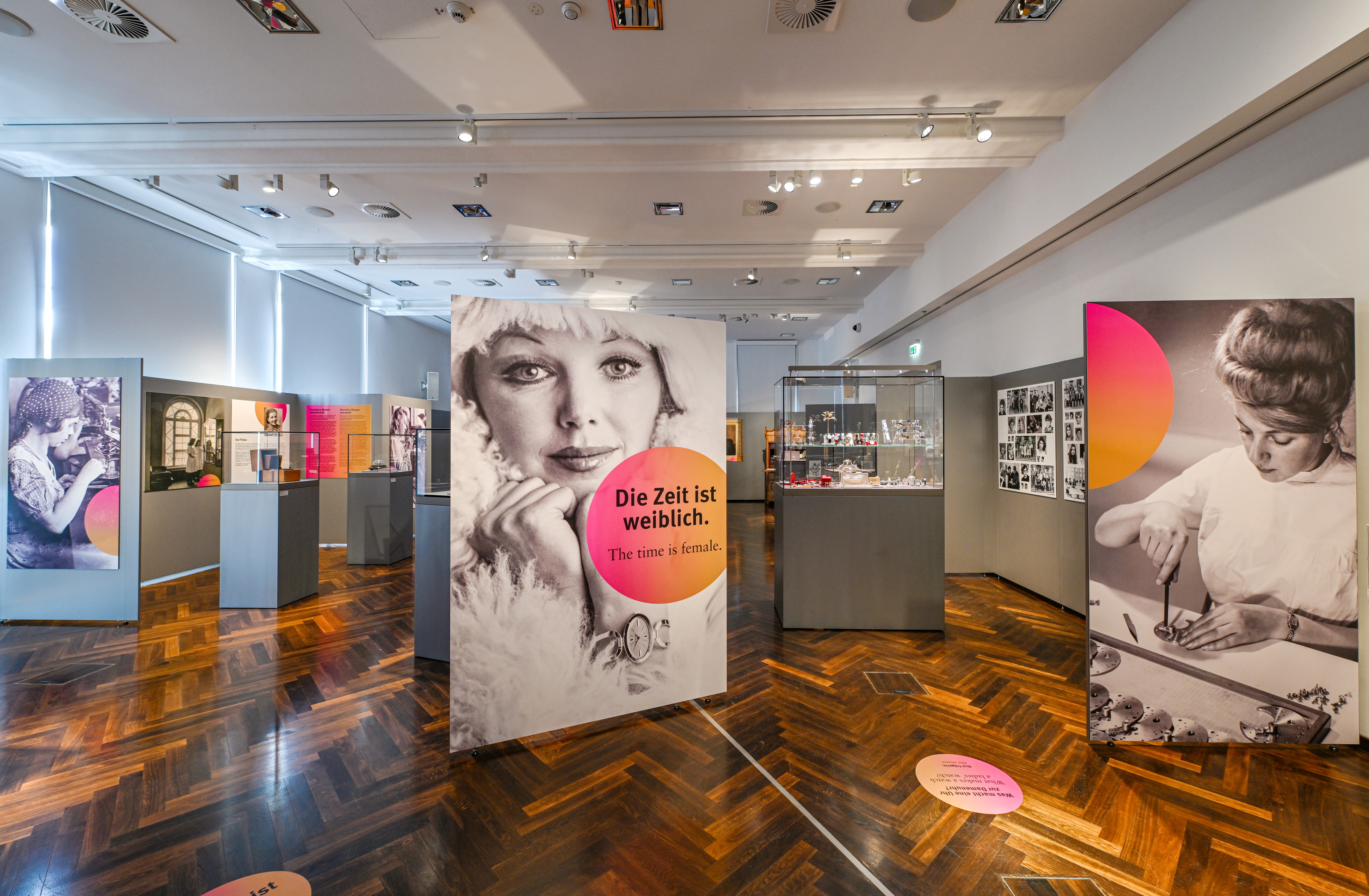 Ein großer Ausstellungsraum mit großen Foto-Stellwänden im Vordergrund und Vitrinen im Hintergrund