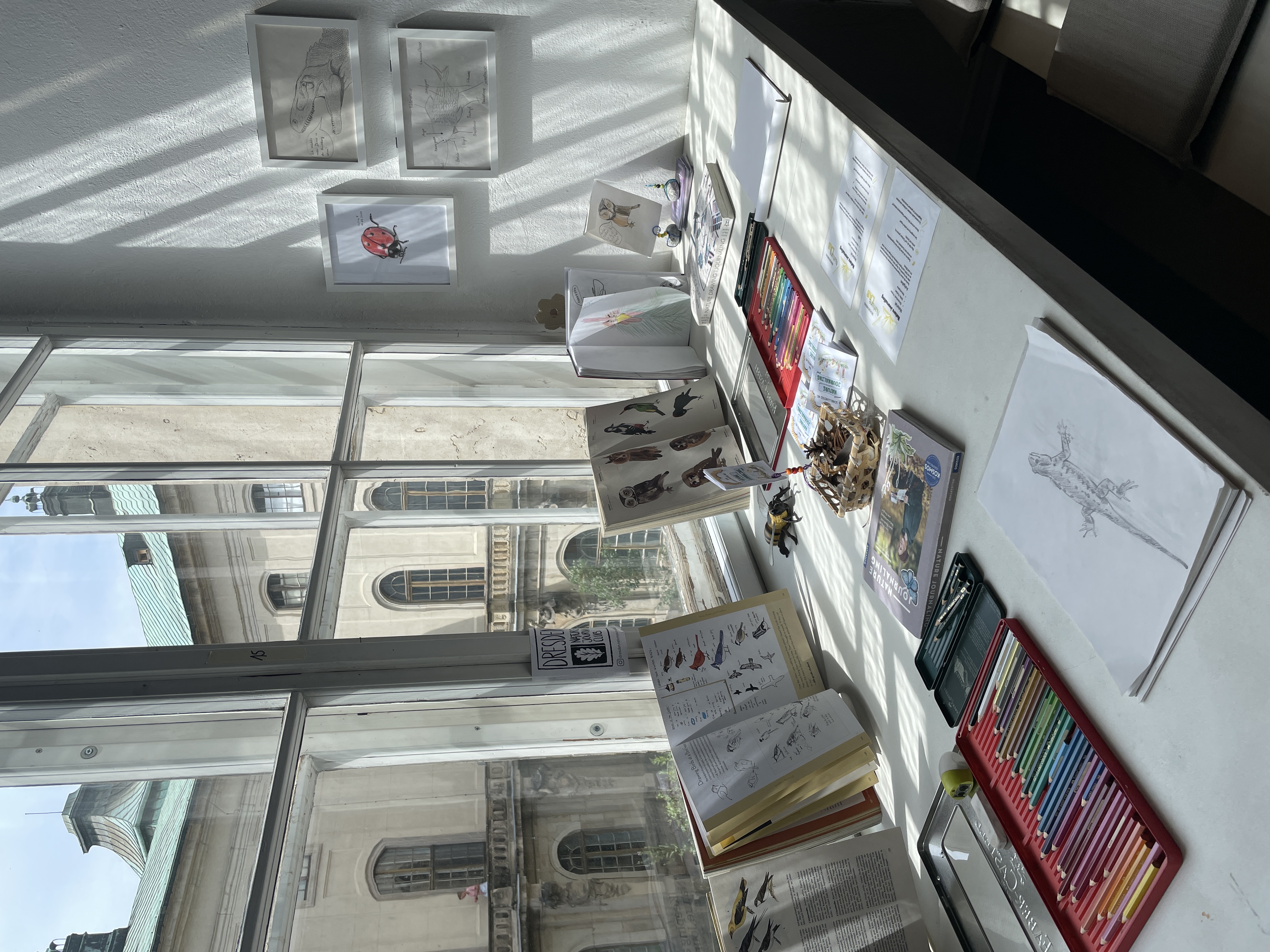Auf einer Fensterbank sind Skizzenhefte und Zeichenmaterialien ausgebreitet.